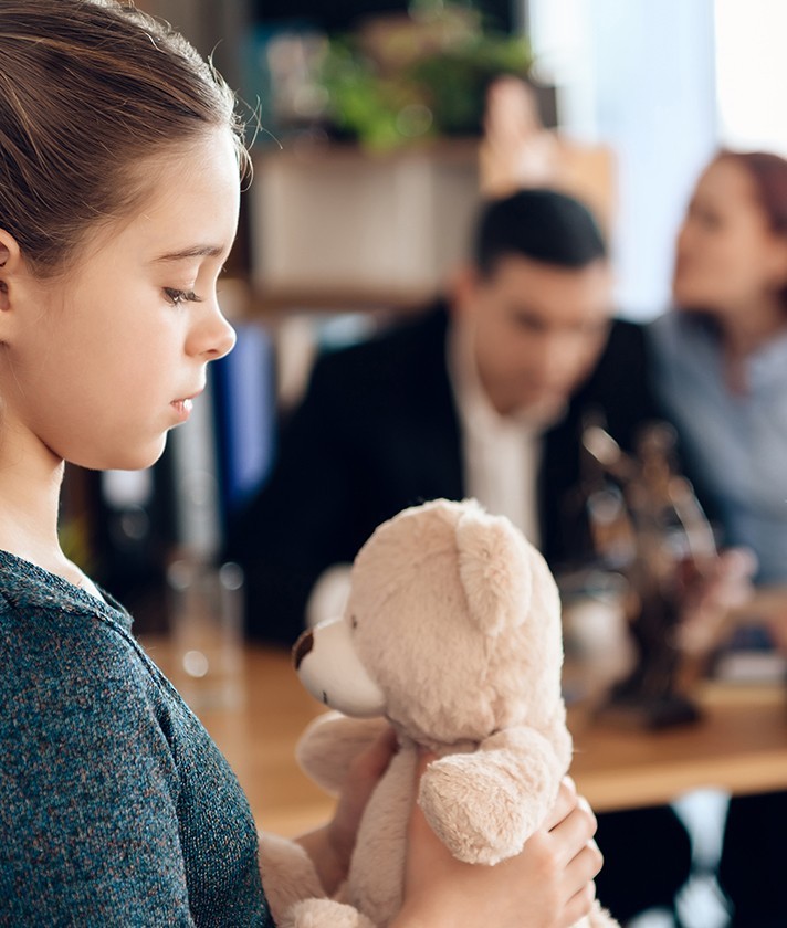 parents talk in background while child looks at teddybear in the foreground